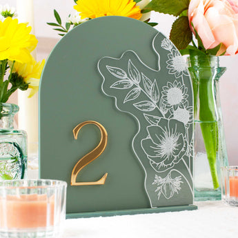Decorative table number with floral design on a green background, surrounded by flowers and candles.