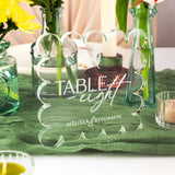 Decorative table sign with 'Table Eight' and personalized names on a green tablecloth.