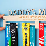 Wooden medal hanger personalised with 'Daddy's Medals', with the included Brushed Aluminium Wall Fixing Mounts shown.