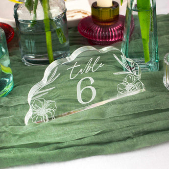 Clear acrylic table number '6' with floral designs on a green tablecloth.